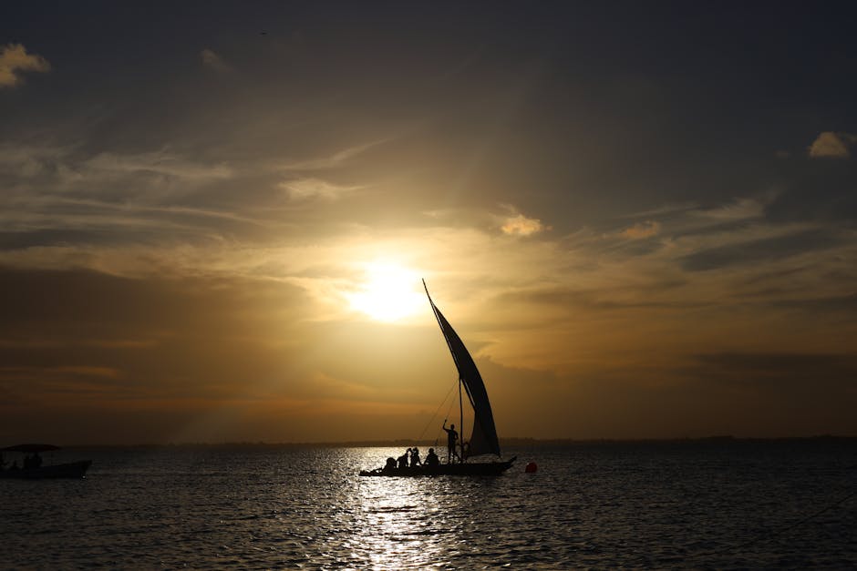 Silhouettes of people on a traditional sailboat sailing at sunset in Zanzibar.