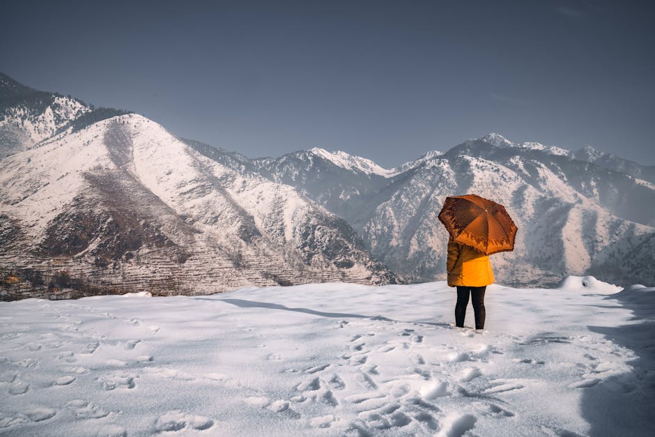A person in warm clothing enjoys a tranquil view of snow-covered mountains in J & K.