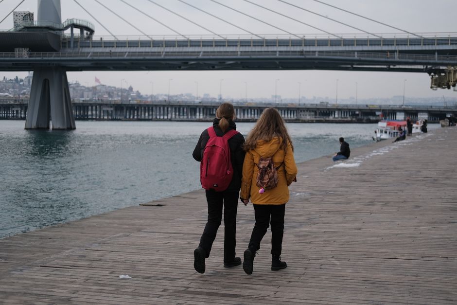 Two women walking on wooden boardwalk under a bridge in Istanbul, Turkey.
