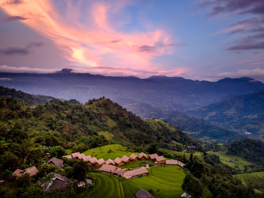 A breathtaking view of terraced fields under a vibrant sunset sky, nestled in rolling hills.