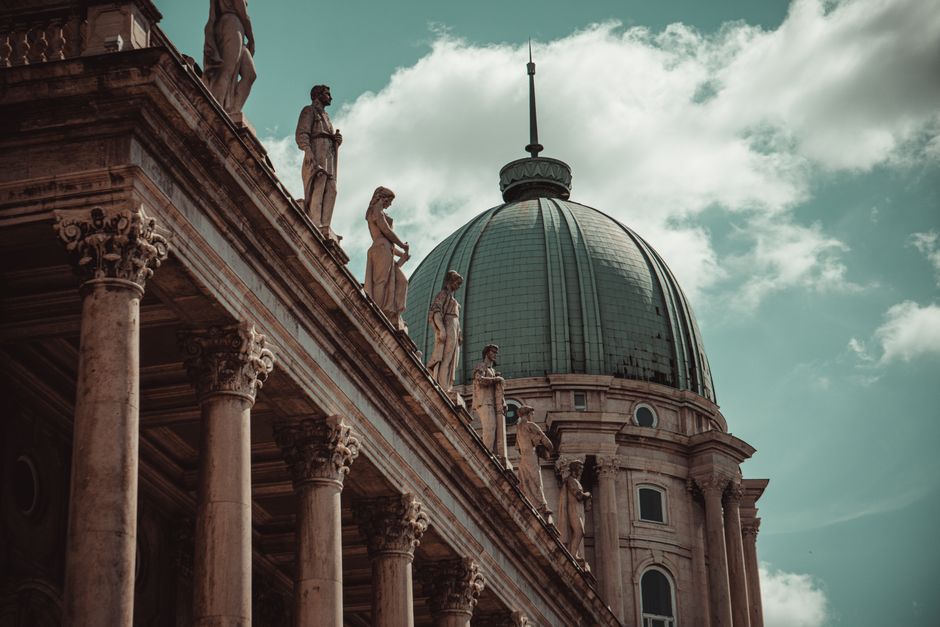 Dramatic view of a dome and statues at a historic Budapest landmark with classic architecture.