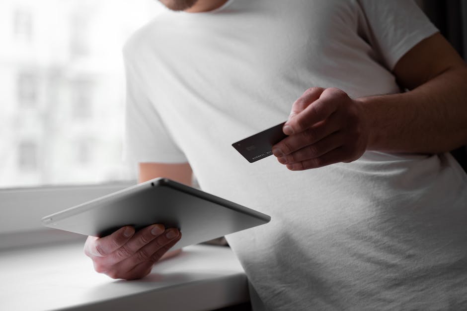 Man in a white shirt using a tablet and credit card indoors for online transaction.