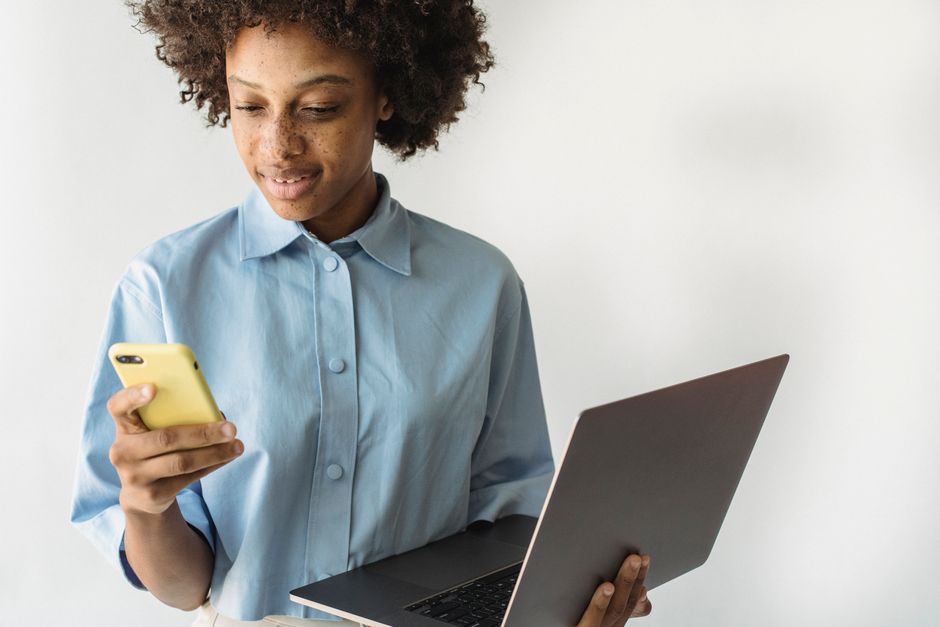 African American woman multitasks with smartphone and laptop, embodying modern technology use.