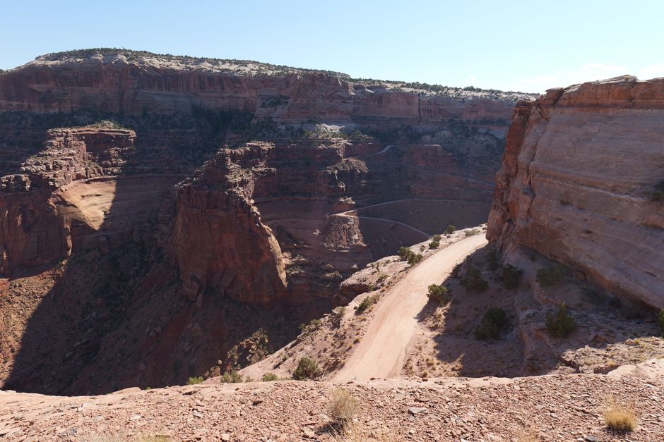 Canyon view showcasing rugged terrain and winding dirt road under clear sky.