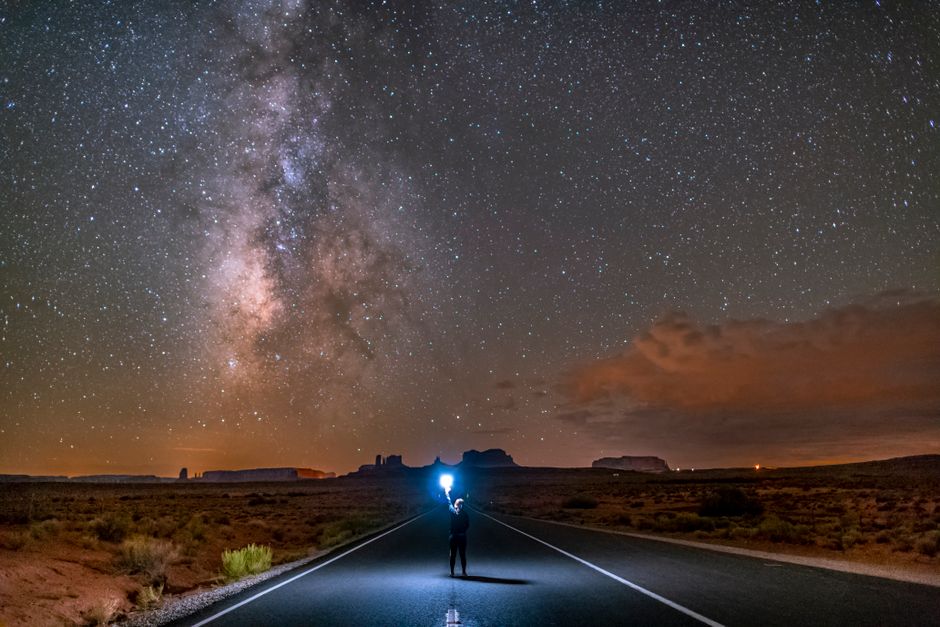 Stunning night view of the Milky Way stretching above a road in Monument Valley, capturing the vastness of the universe.