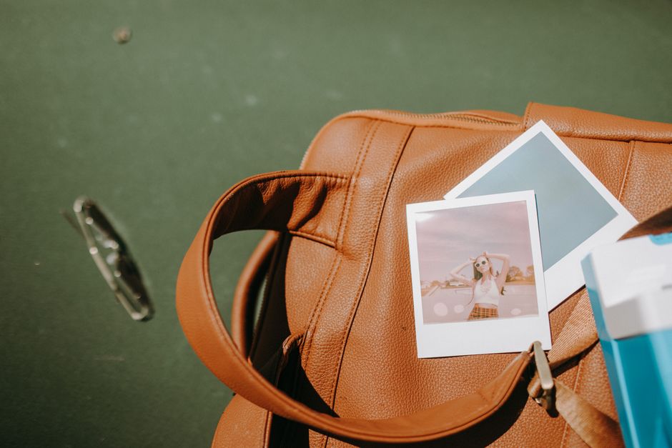 Close-up of polaroid pictures placed on a tan leather bag outdoors.