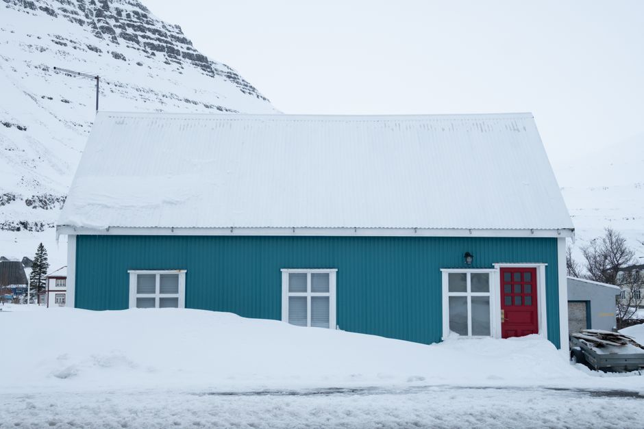 A blue house with red door surrounded by deep snow in a Nordic winter scene.