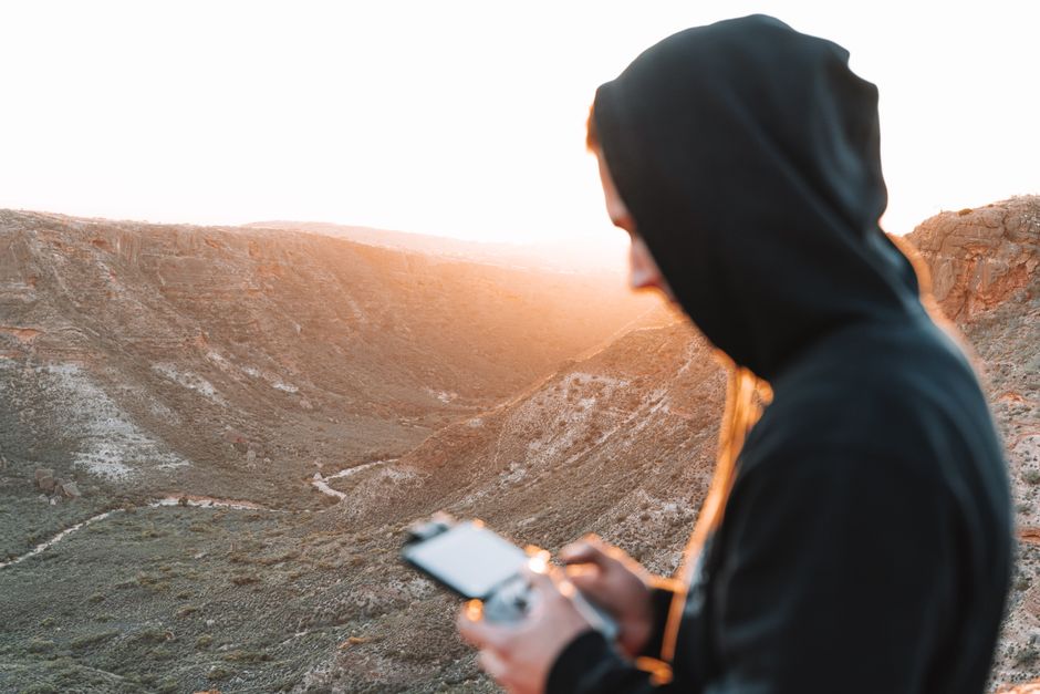 Person in hoodie controlling a drone in a beautiful canyon setting at sunset.
