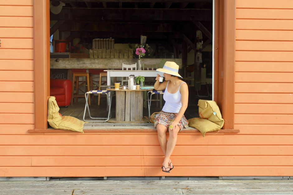 A woman in a sun hat sips coffee at Tathra Wharf Cafe, NSW, embodying a relaxed, summer vibe.