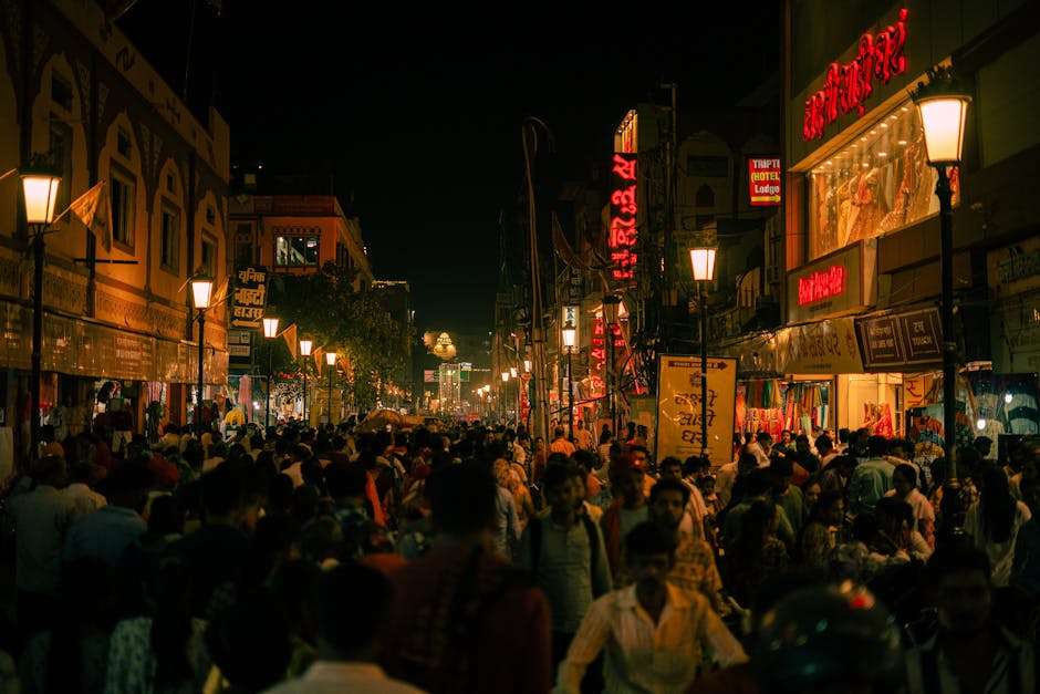 A bustling street in Varanasi, India, illuminated at night with crowds and vibrant signs.
