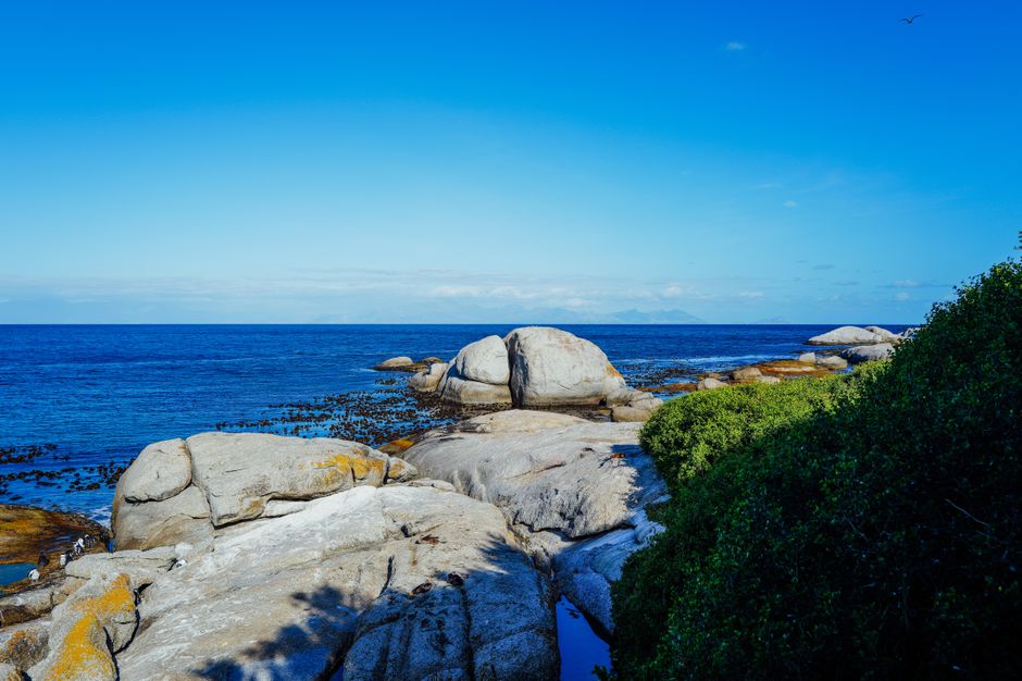 A tranquil rocky beach scene with a vibrant blue ocean under a clear sky.