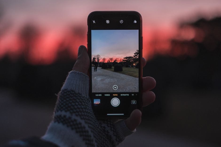 A hand holds a smartphone capturing a stunning sunset scene during twilight.