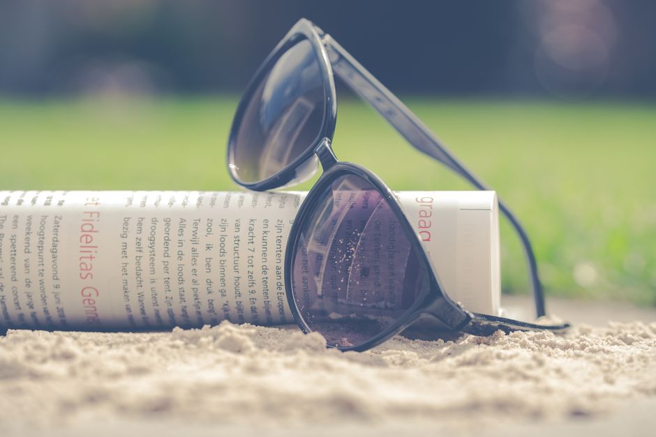 Chic black sunglasses resting with a rolled newspaper in the sand on a sunny summer day.