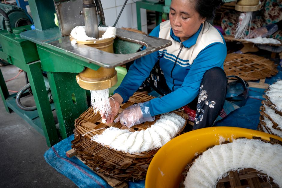 Asian lady making noodle near metal machine and wooden covers in factory in Vietnam