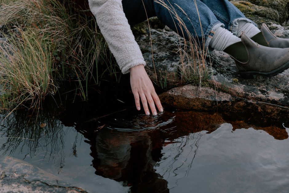 A peaceful moment by the lake with a person gently touching the water, creating a serene reflection.